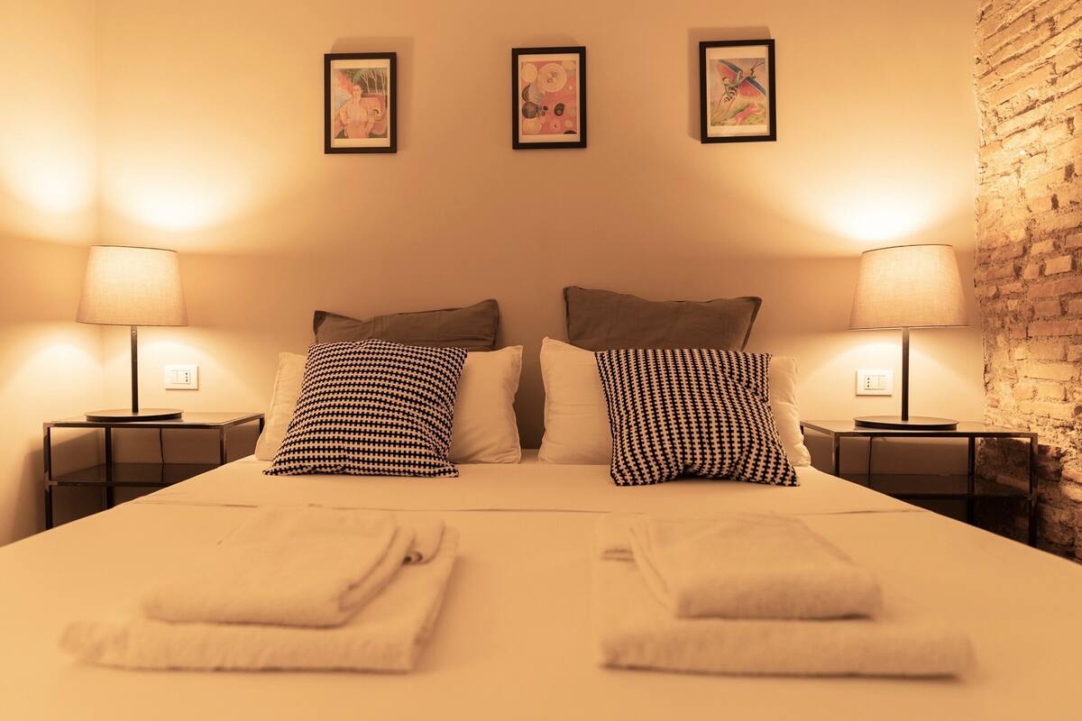 Une chambre d’hôtel avec un lit, deux tables de chevet, deux lampes et trois tableaux encadrés au mur.