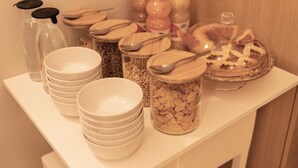 Un comptoir de petit-déjeuner avec des assiettes blanches empilées, des bocaux de céréales et des bouteilles de jus de fruits.