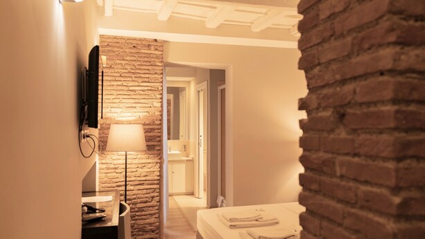 Une chambre d’hôtel avec un mur en briques, un lit où les serviettes sont soigneusement pliées, une table de chevet et une lampe.