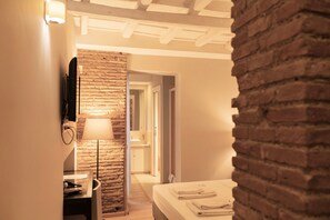 Habitación de hotel con pared de ladrillo, cama con toallas ordenadas, mesita de noche y lámpara.