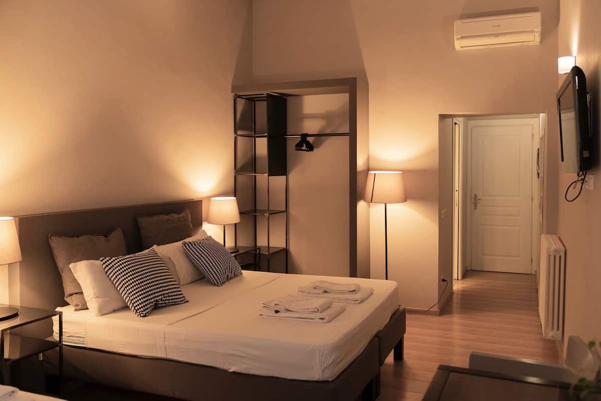 Une chambre d’hôtel comprenant un lit, des lampes de chevet, une armoire, un miroir et une porte donnant sur une autre pièce.