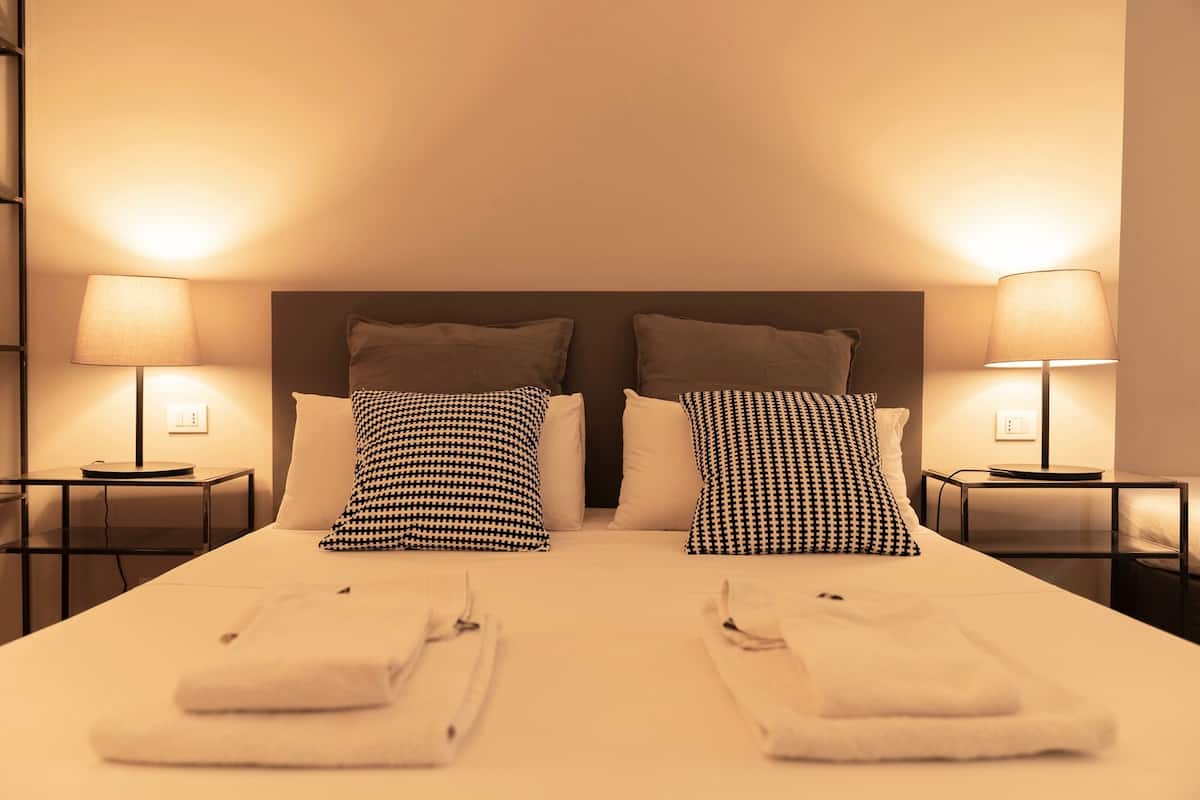 Un lit bien fait, avec deux oreillers, deux tables de chevet avec des lampes et une tête de lit.
