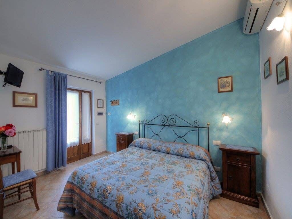 A bedroom with a bed, a desk with a chair, a window with curtains, and wall-mounted lights.