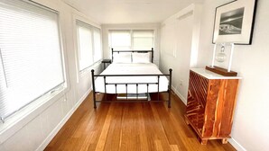 A bedroom with a bed, wooden floor, white walls, and a small wooden dresser. - 9819 Shore - Beachfront on Primehook Beach. (Milford)