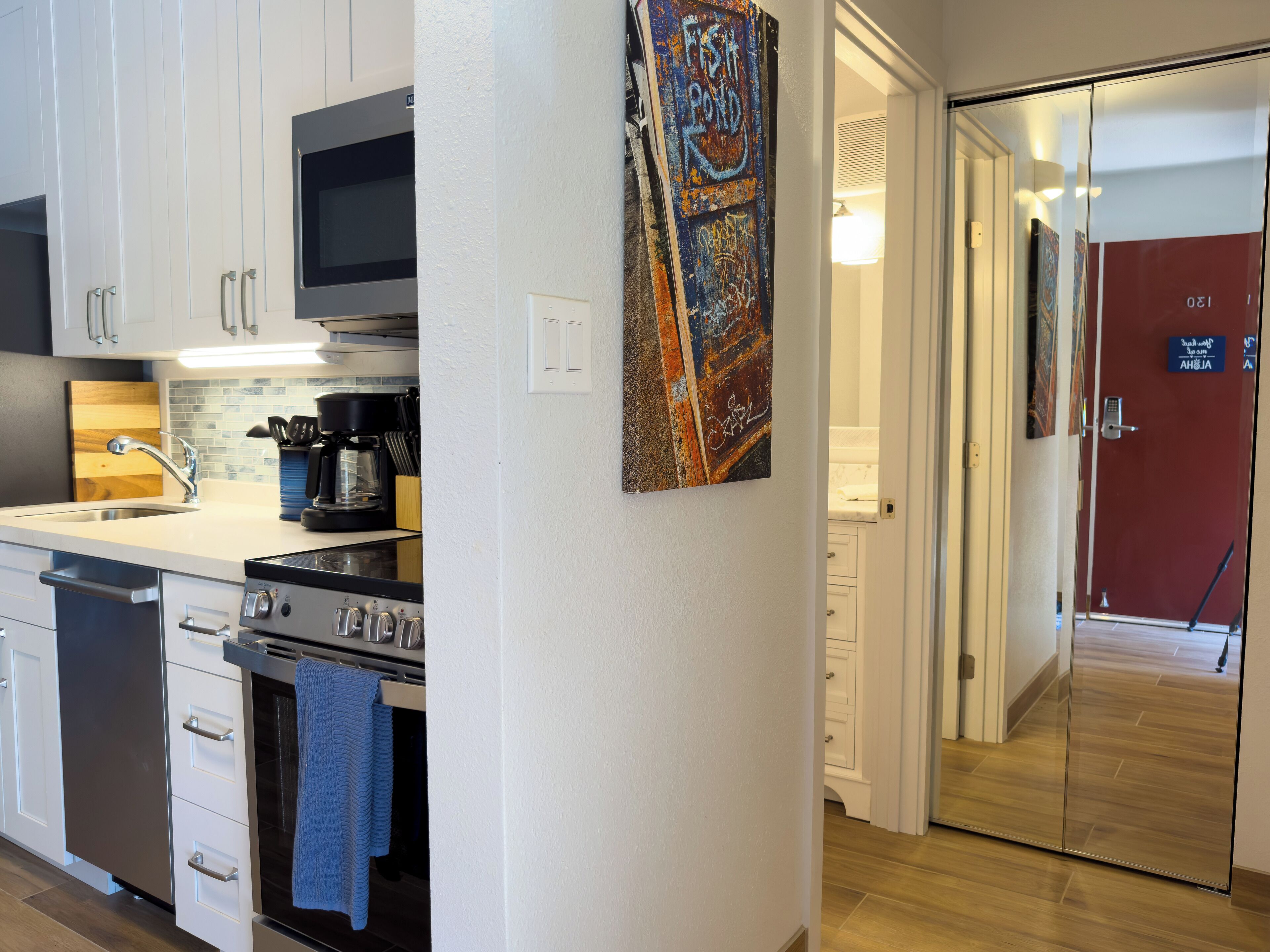 A modern kitchen with stainless steel appliances, a microwave, and a coffee maker. There is a blue towel hanging on the oven handle.