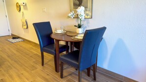 A dining area with a wooden table, two blue chairs, a small potted plant, and a framed picture on the wall. - Newly remodeled studio, jacuzzi and pool (Kihei)