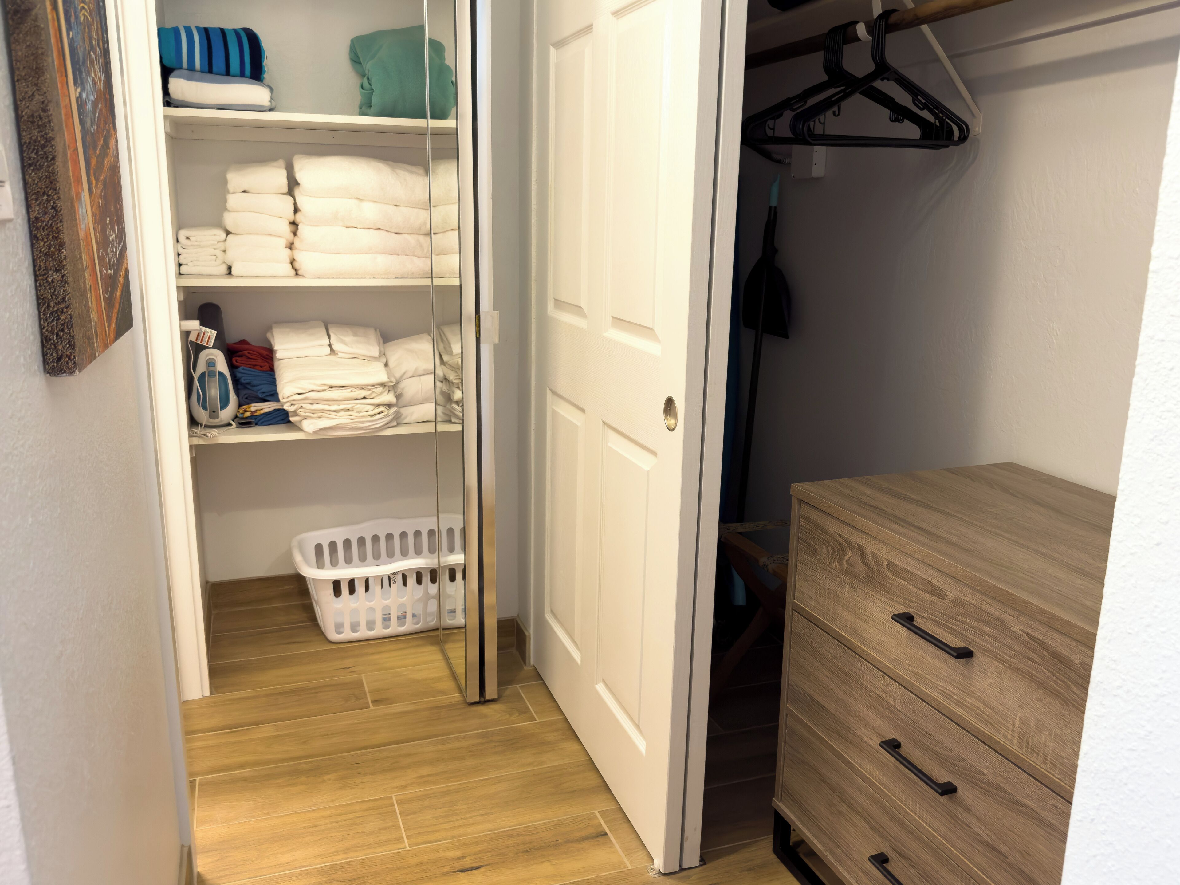 Ein begehbarer Kleiderschrank mit Regalen für gefaltete Kleidung, einem Wäschekorb und einer Holzkommode mit Schubladen.