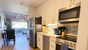 A modern kitchen with stainless steel appliances, a built-in oven, and a dining area with a table and chairs. - Newly remodeled studio, jacuzzi and pool (Kihei)
