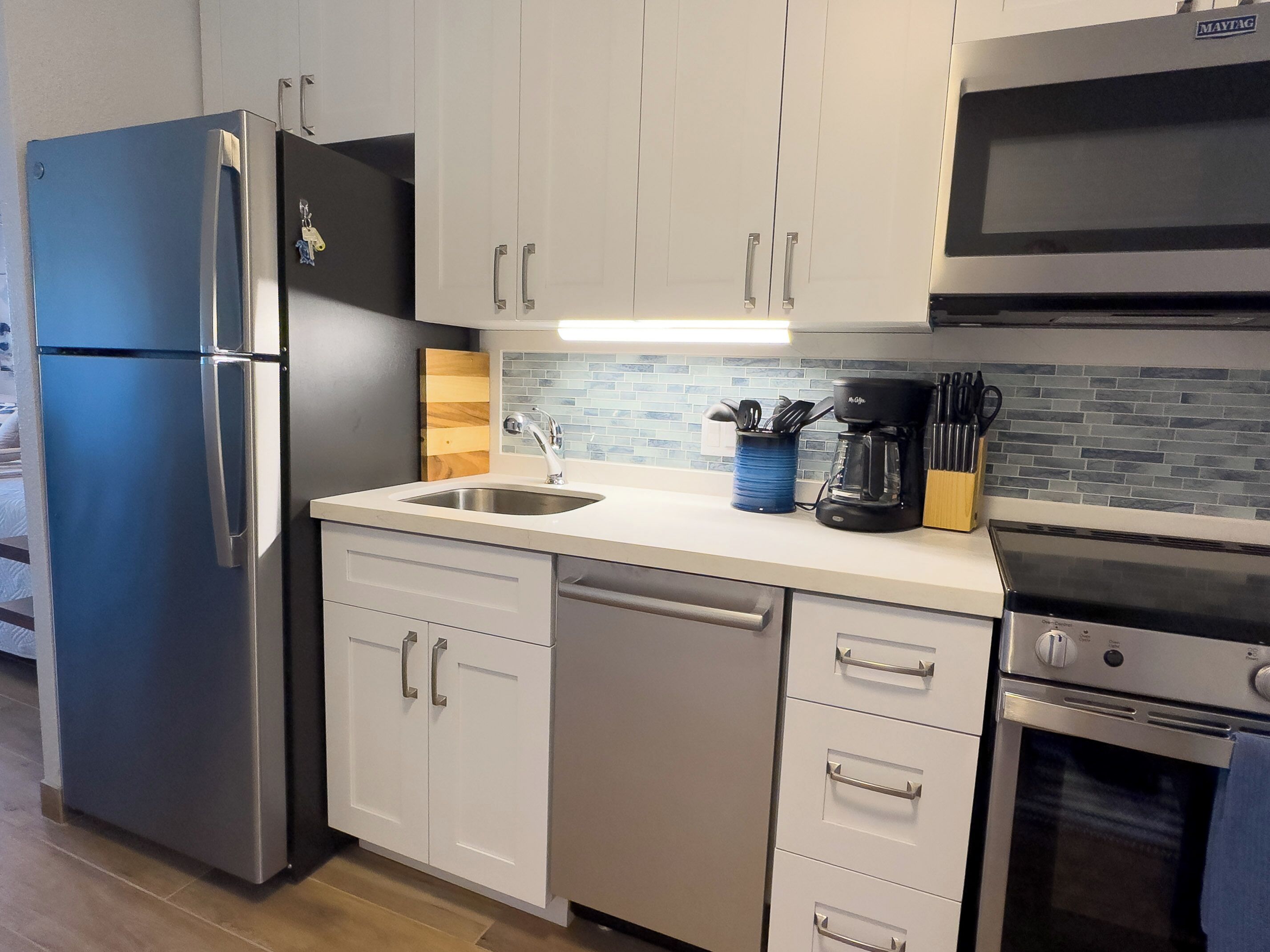 Una cocina moderna con electrodomésticos de acero inoxidable, armarios blancos y salpicadero de azulejos.