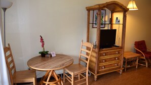A room with a round wooden table, two wooden chairs, a wooden cabinet with a television, and a red chair.