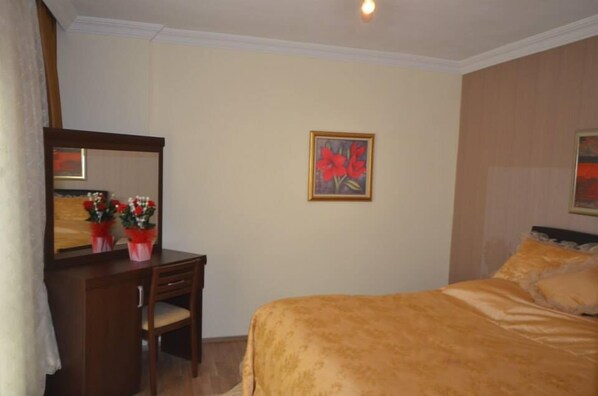 A hotel room with a bed, a desk with a chair, a mirror, and a painting on the wall. - Evrim Hotel (Hacibektas)