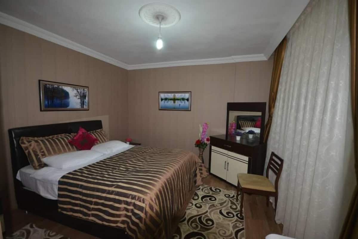 A hotel room with a bed, a desk, a chair, a wardrobe, and two framed pictures on the wall.