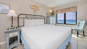 A bedroom with a bed, nightstands, a lamp, a chair, a window with a view, and a sign reading 'BEACH HOUSE'. - BEACH FRONT! Condo in HIGH Demand! (Gulf Shores)