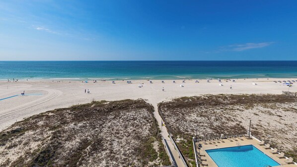 A beach resort with a swimming pool, beach umbrellas, and a clear view of the ocean. - BEACH FRONT! Condo in HIGH Demand! (Gulf Shores)