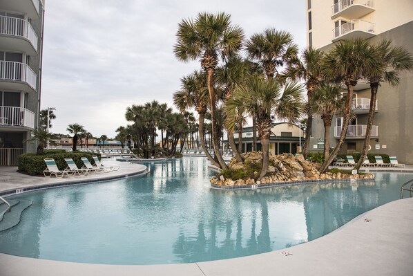 A swimming pool with lounge chairs and palm trees, surrounded by multi-story buildings.