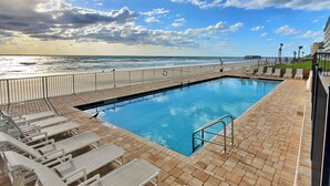 Une piscine avec vue sur l’océan, une terrasse avec des chaises longues et un bâtiment en arrière-plan.