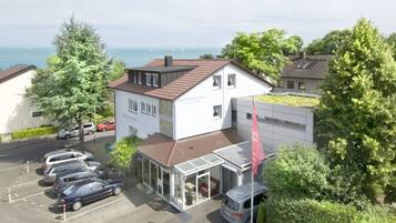 Ein Gebäude mit Glastür, parkenden Autos und Blick auf das Meer.