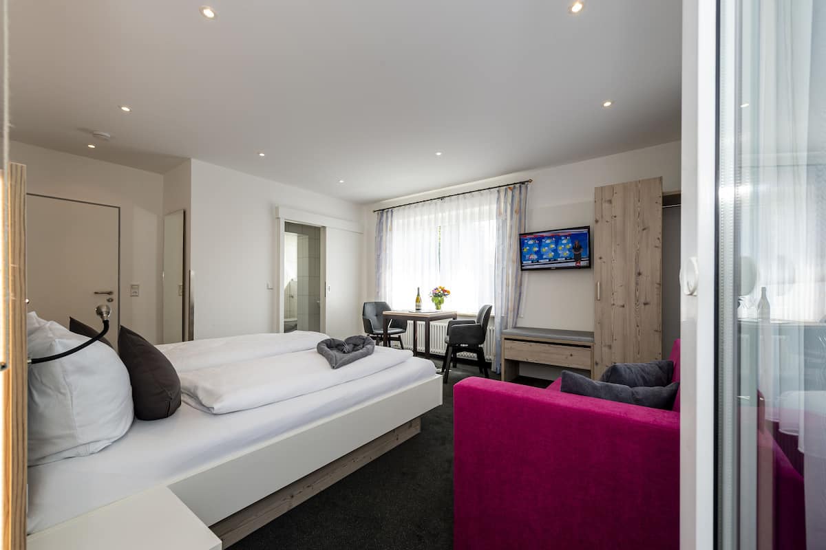 A hotel room with a bed, a desk, a chair, a TV, and a window with curtains.