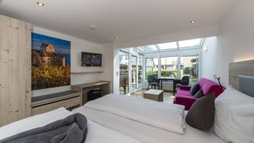 Ein modernes Hotelzimmer mit einem großen Bett, einem Schreibtisch, einem Sessel und einem Sofa. Ein großes Fenster bietet einen Blick nach draußen.