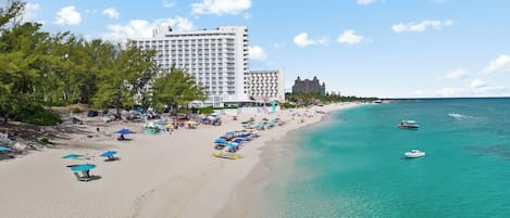 A beach with a hotel, clear turquoise water, and a boat.