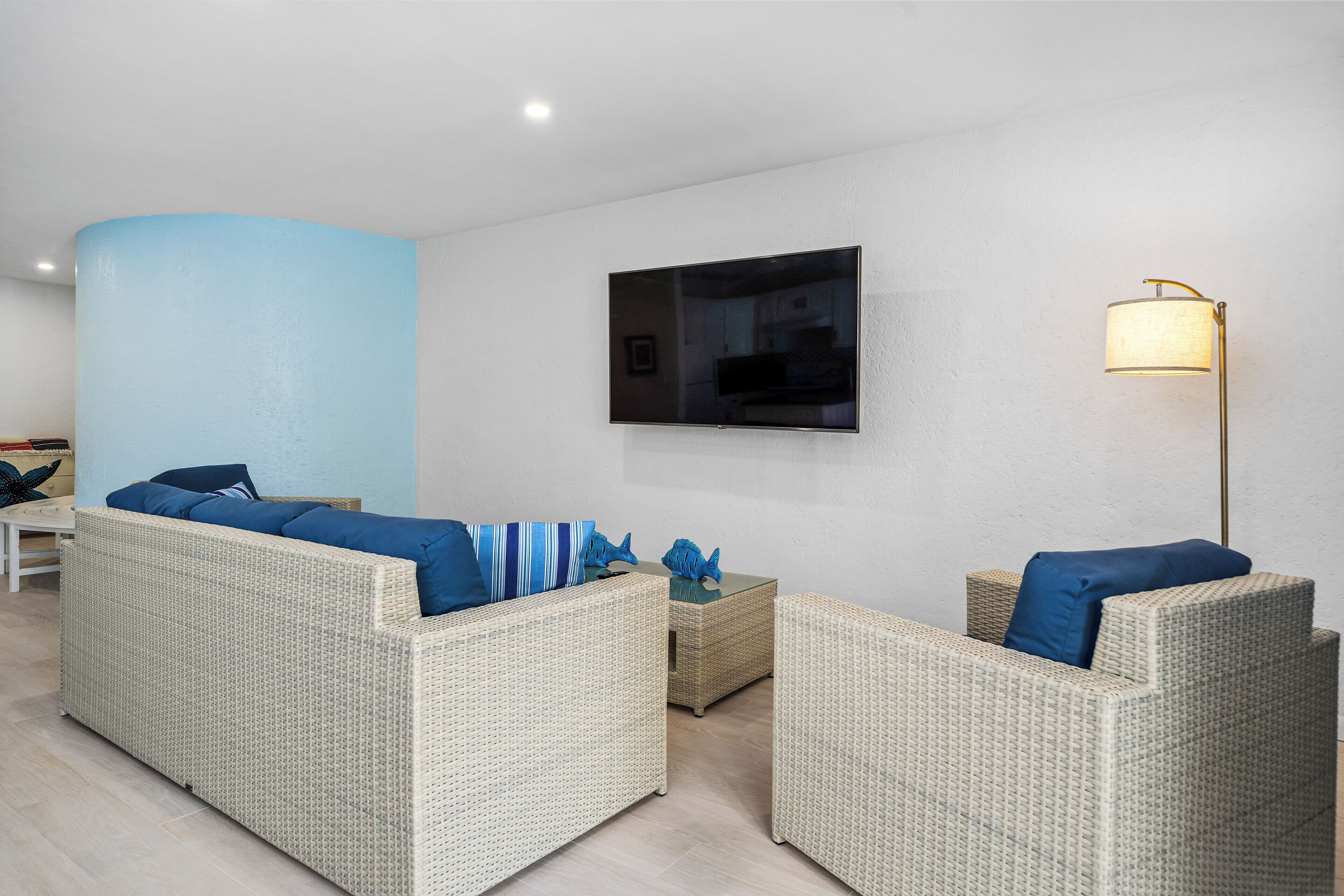 A modern living room with wicker furniture, a flat-screen TV, and a floor lamp.