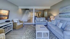 A modern living room with a flat-screen TV, wicker furniture, a light blue sofa, and a staircase leading to another room.