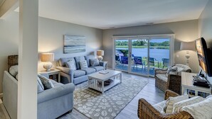 A spacious living room with a large sofa, a coffee table, and a view of a lake through glass doors.