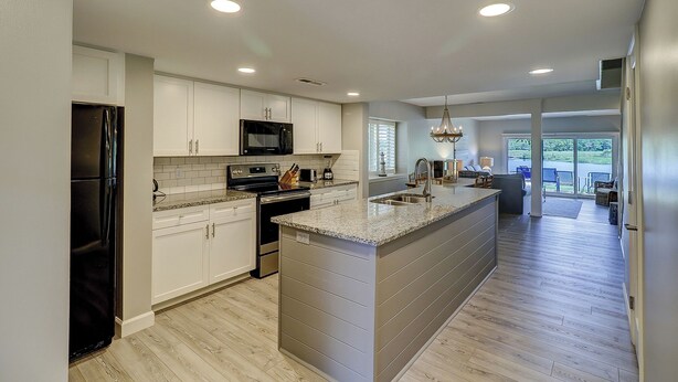 A modern kitchen with white cabinets, a black refrigerator, stainless steel appliances, and a large island with a sink.