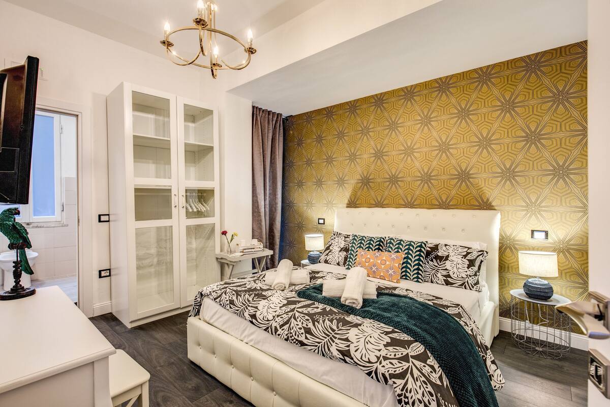 Un dormitorio con una cama grande, un armario, una araña y papel tapiz estampado.