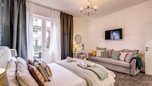 Habitación de hotel con cama, sofá, televisión y ventana con cortinas.