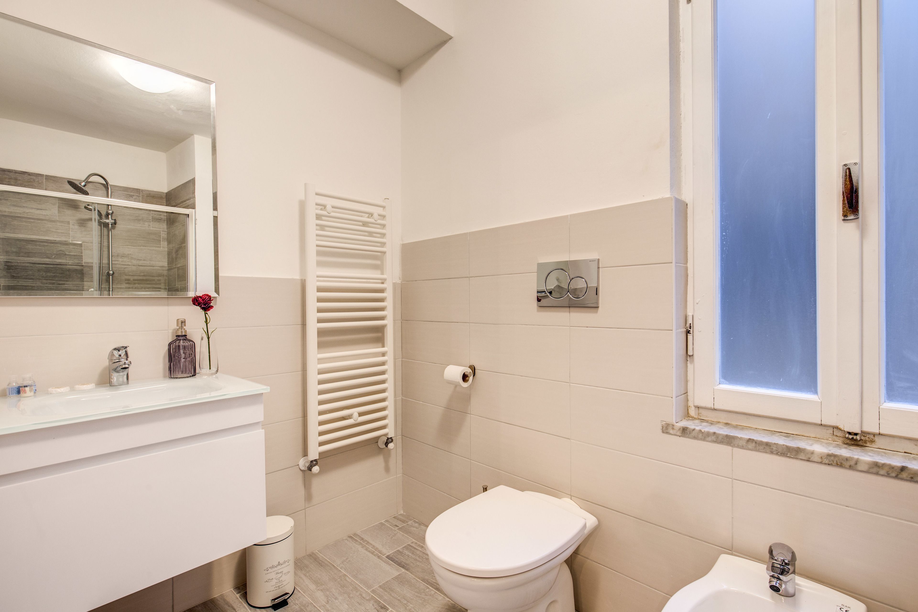 Un baño con lavamanos blanco, inodoro, ducha y ventana.
