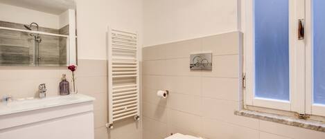 Un baño con lavamanos blanco, inodoro, ducha y ventana.