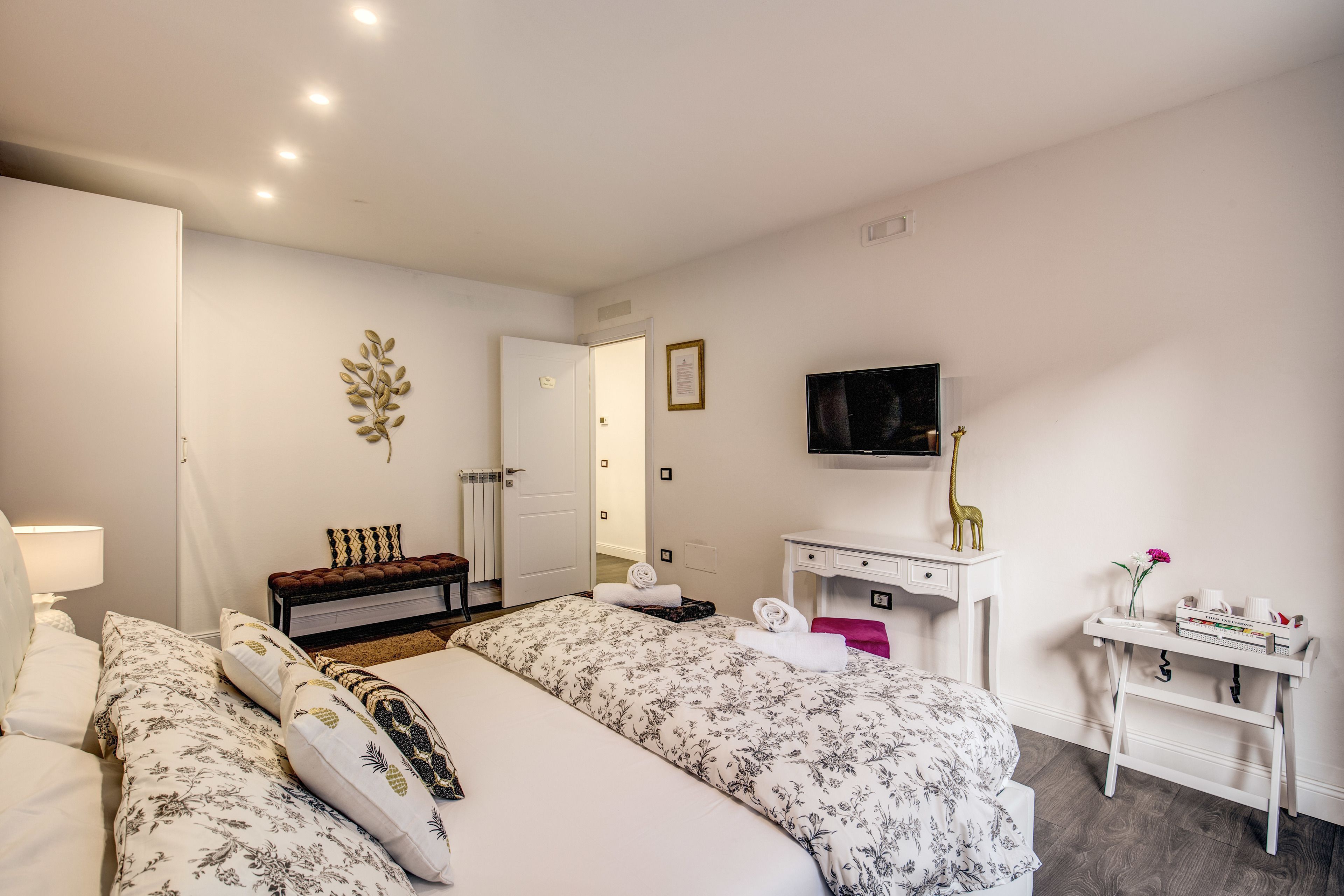 Habitación de hotel con dos camas, un escritorio, un televisor y una pequeña mesa con un florero.
