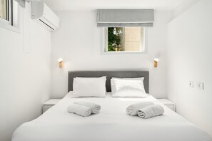 A modern hotel room with a large bed, two bedside tables, a window with a view, and an air conditioning unit.