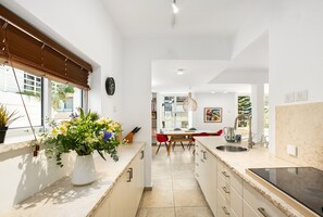 A modern kitchen with a central island, a dining area with red chairs, and a view of the outdoors through large windows.