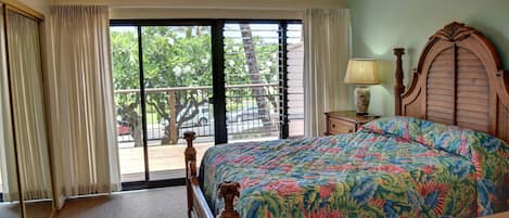 A bedroom with a large bed, a wooden headboard, a nightstand with a lamp, and a view of the outdoors through a sliding glass door.