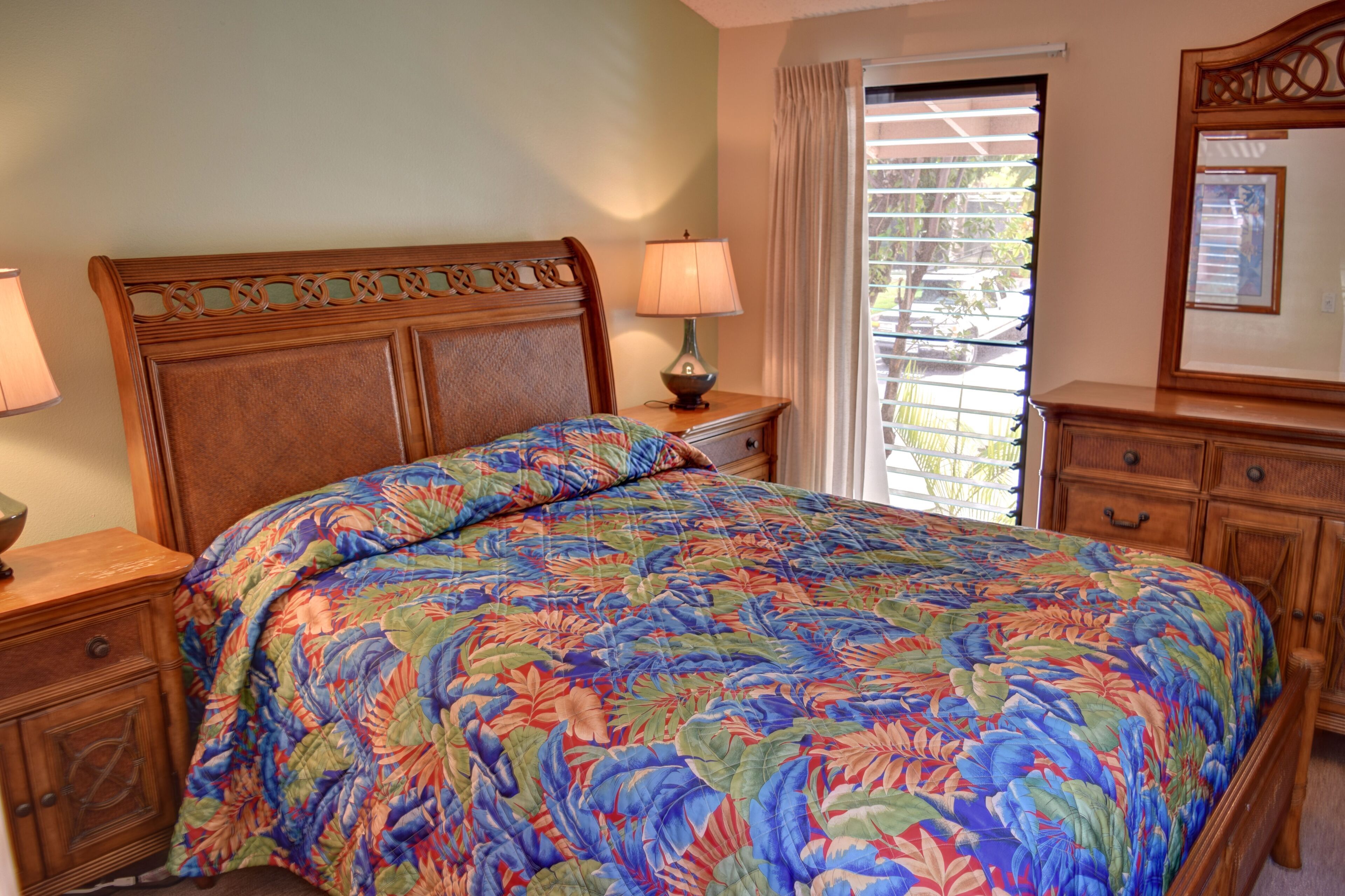 A bedroom with a floral bedspread, wooden headboard, bedside lamps, and a window with blinds.
