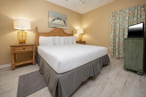 Habitación de hotel con una cama, dos lámparas de noche, un cuadro, un televisor y una cortina con estampado floral.