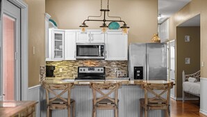 Una cocina con gabinetes blancos, un refrigerador de acero inoxidable, un microondas empotrado, una cafetera e isla de madera con taburetes de bar.