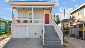 Ein zweistöckiges Haus mit roter Tür, einer Veranda und einer Treppe, die zur Garage führt.