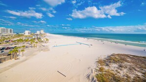 Una playa con cielo despejado, orilla de arena y edificios al fondo.