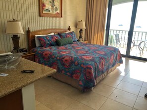 A hotel room with a bed, two bedside lamps, a framed picture on the wall, and a balcony with a railing. - 6 th floor ocean front condo Outstanding Views! Weekly discounts available (Lahaina)