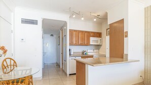 A kitchen with wooden cabinets, a microwave, a stove, and a sink. There is a glass table with chairs and a door leading to another room. - 6 th floor ocean front condo Outstanding Views! Weekly discounts available  (Lahaina)