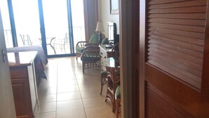 A hotel room with a wooden door, a dining area with chairs and a table, and a view through large windows. - 6 th floor ocean front condo Outstanding Views! Weekly discounts available  (Lahaina)