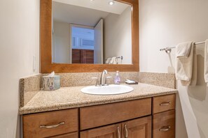 A bathroom with a granite countertop, a white sink, a mirror, and wooden cabinets. - 6 th floor ocean front condo Outstanding Views! Weekly discounts available (Lahaina)