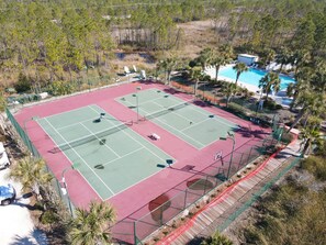 Uma quadra de tênis ao ar livre com piscina e palmeiras.