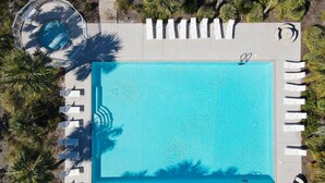 Eine Vogelperspektive auf einen rechteckigen Swimmingpool, umgeben von weißen Liegestühlen und einer kleinen Terrassenfläche.