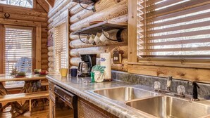 A wooden cabin interior with a kitchen area featuring a large sink, a coffee maker, and wooden logs as wall decor. - ER45 - Tin Pan Alley - Great location. Just across from swimming pool! (Pigeon Forge)