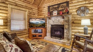 A log cabin interior with a stone fireplace, wooden walls, a mounted clock, and a television. - ER45 - Tin Pan Alley - Great location. Just across from swimming pool! (Pigeon Forge)