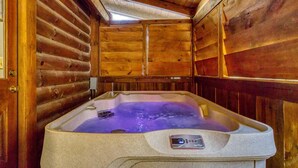 A log cabin interior with a stone hot tub, wooden walls, and a sloped ceiling. - ER204 - Dream Catcher  Great location! - Close to town! (Pigeon Forge)